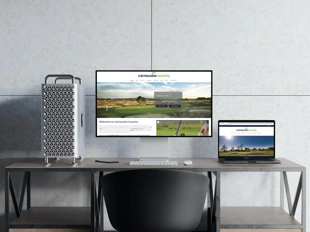 A computer monitor and laptop screen in a stark modern office showing the Carnoustie Country website